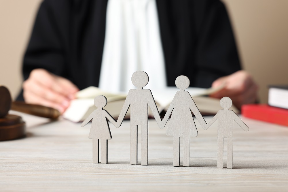 Family law. Judge with book sitting at white wooden table, focus on figure of parents and children Family law. Judge with book sitting at white wooden table, focus on figure of parents and children